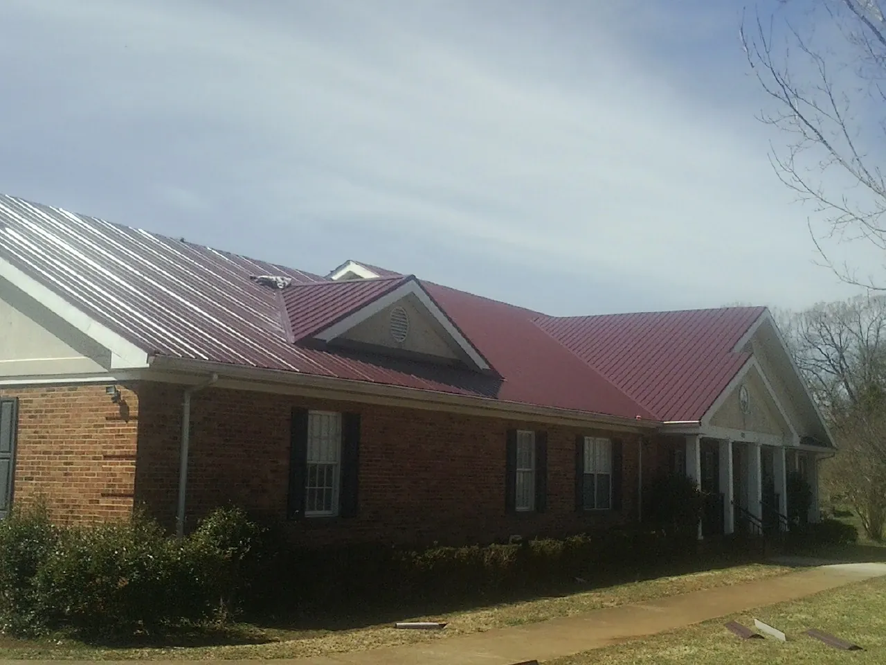Red metal roof with gabled entries on a long brick building, from a Hail Damage Roof Repair job in Faulkner