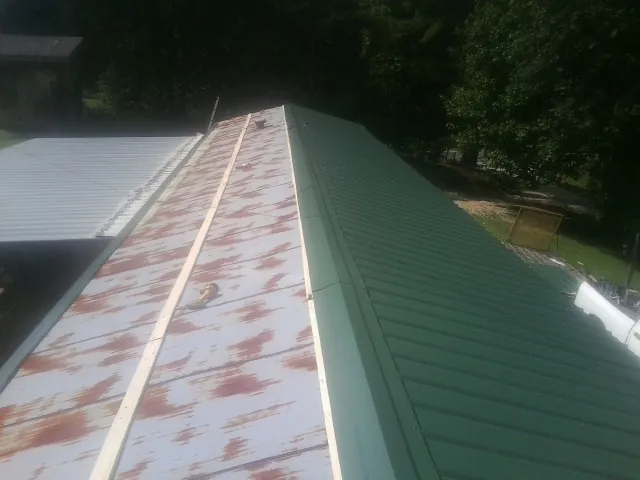 Old rusted panels beside newly installed green metal roofing — Wind Damage Roof Repair by Roofing Brothers in Faulkner