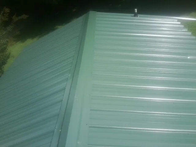 New green metal panels meeting at the ridge of a roof — Flat Roof Repair work by our crew in Faulkner