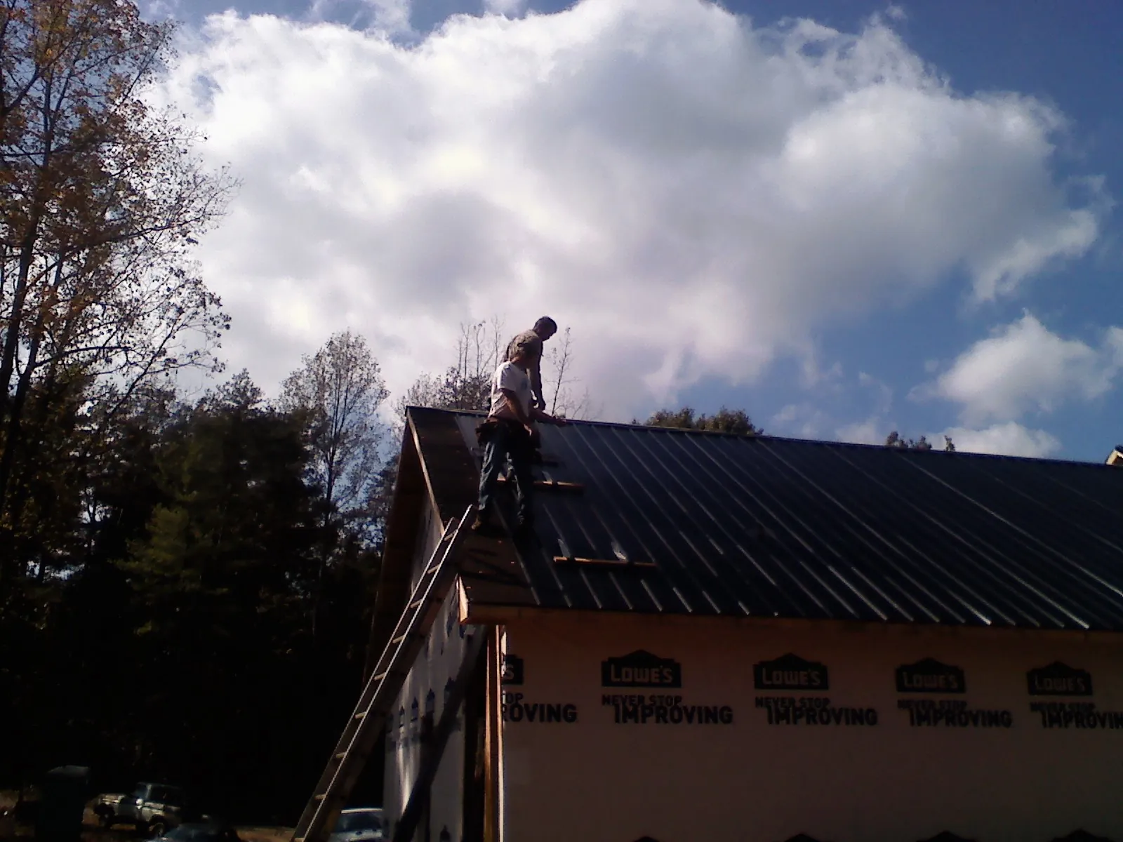 Roofer fastening dark metal panels high against a cloudy sky, from a Roof Inspection job in Faulkner