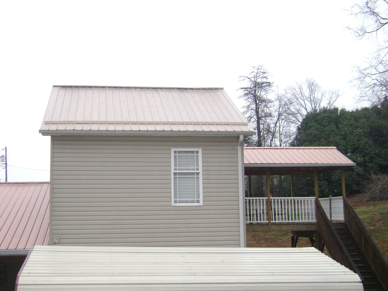 Tan metal roofs on a two story addition and attached porch, from a Roof Replacement job in Faulkner